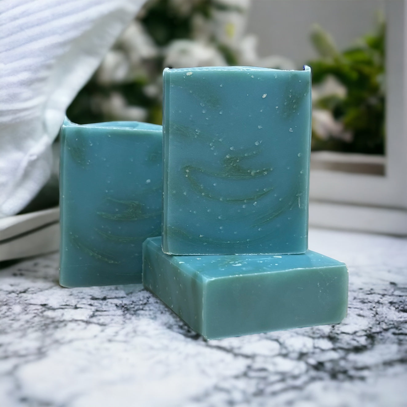 A blue and green rectangular bar of soap on a marble countertop, with a plant in the background.