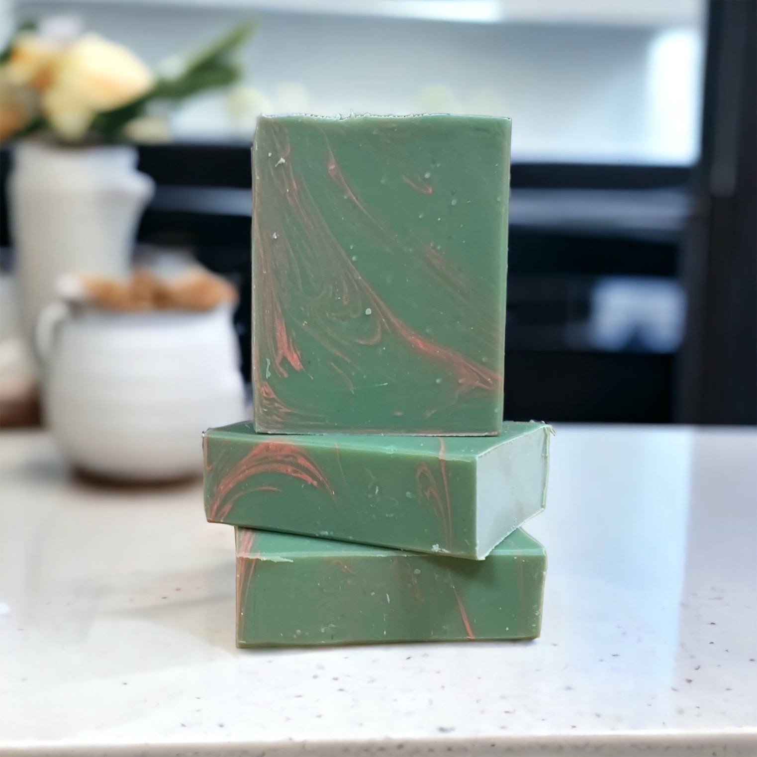 A green and pink rectangular bar of soap on a white countertop with a vase of flowers in the background.