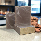 A brown and white rectangular bar of soap on a countertop with almonds in the background.