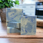 A blue and white rectangular bar of soap on a wooden countertop with a plant in the background.
