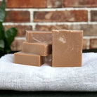 A brown and white rectangular bar of soap on a cloth with a plant and a brick wall in the background.